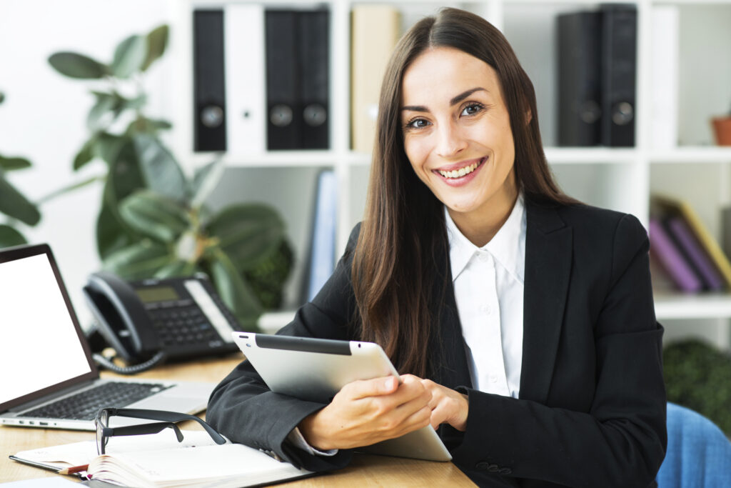 Retrato empresaria joven que sienta escritorio que sostiene tableta digital su mano